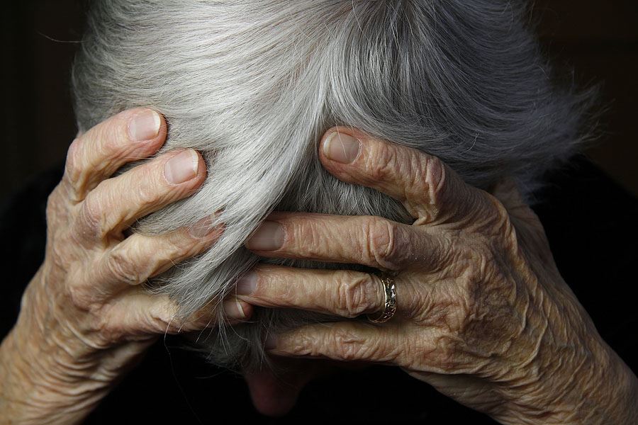 Elderly woman holding her head in her hands.