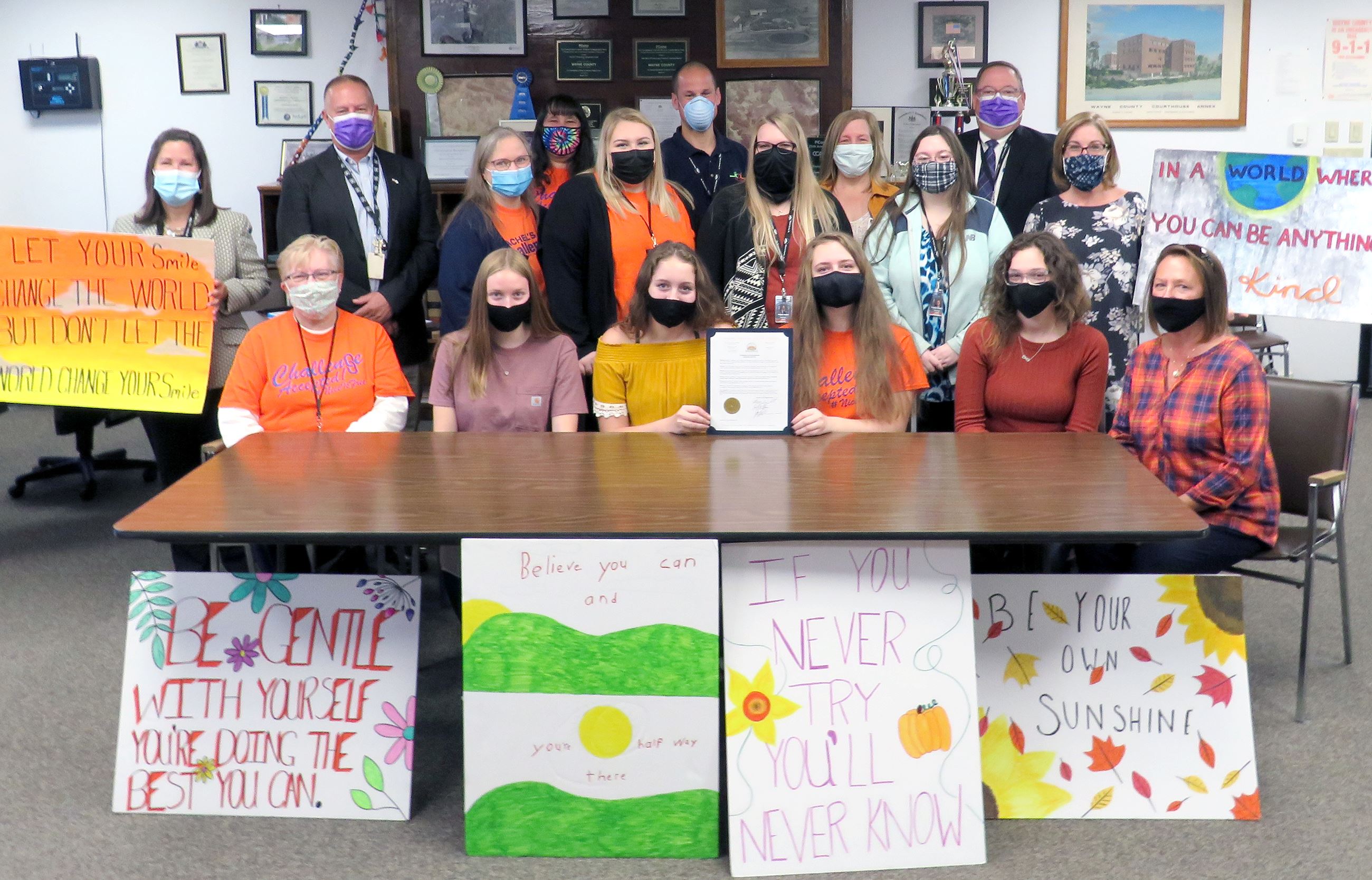 A group of Rachel's Challenge Committee Member pose with the Commissioners and kindness posters.